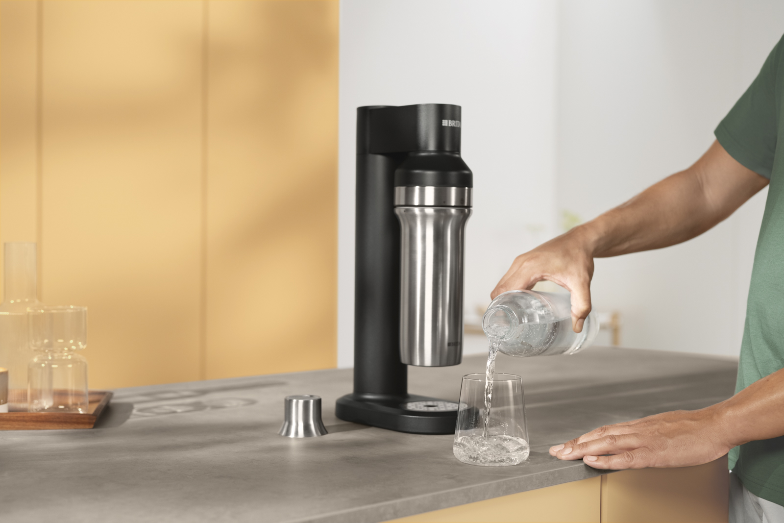 Ein Mann gießt sich ein Glas Wasser ein und steht neben dem BRITA sodaTRIO.